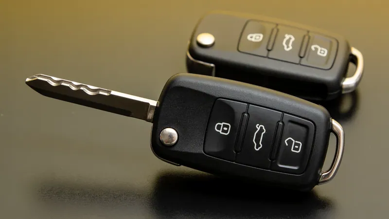 Duas chaves canivete automotivas pretas com botões de travar, porta-malas e destravar: uma aberta com lâmina de aço fresada e outra fechada ao fundo